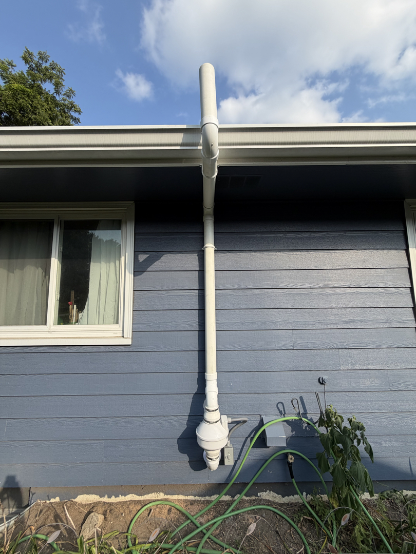 Radon mitigation pipe run, blue siding background